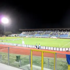 Wieczorny mecz na stadionie w San Marino. Piłkarze biegają po zielonej murawie, a trybuny wypełnia publiczność.