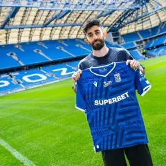 Ali Gholizadeh prezentuje nową koszulkę Lecha Poznań na tle stadionu.