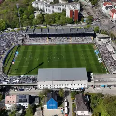 Widok z lotu ptaka na tętniący życiem tsv monachium stadion, pełen kibiców. Piłkarze rozgrywają mecz na zielonej murawie.