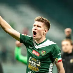 Piłkarz w zielonej koszulce z podniesioną pięścią świętuje awans do ekstraklasy.