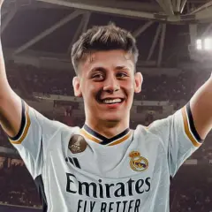 Uśmiechnięty Arda Güler w koszulce Realu Madryt z podniesionymi rękami, świętuje sukces na tle trybun stadionu.