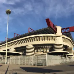 Stadion AC Milan, San Siro, z charakterystycznymi czerwonymi elementami dachu i kulistą latarnią, prezentuje się imponująco na tle błękitnego nieba.