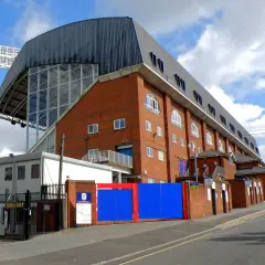 Widok na ceglany budynek stadionu Crystal Palace z charakterystycznym zadaszeniem i przeszkloną ścianą.