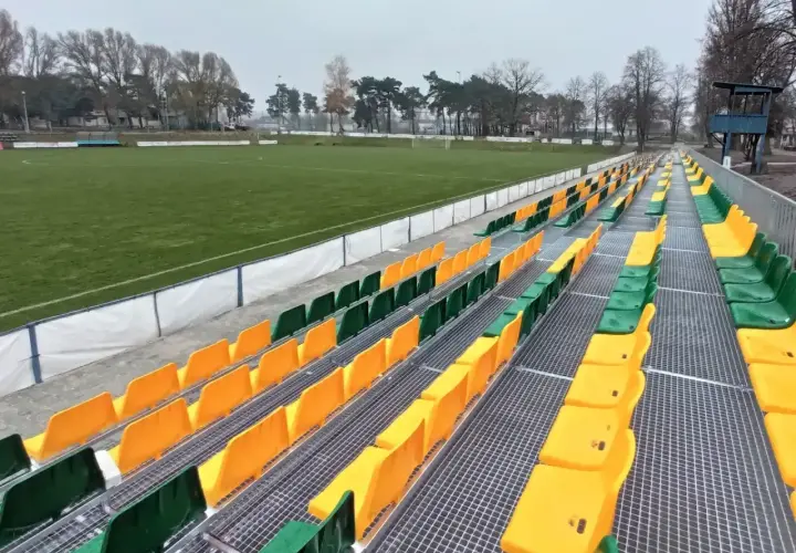 Puste trybuny stadionu Lechii Zielona Góra, z rzędami zielonych i żółtych krzesełek.