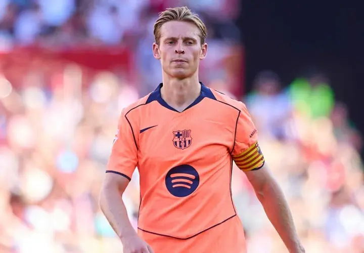 Frenkie de Jong w pomarańczowej koszulce FC Barcelony z opaską kapitana na ramieniu, skupiony na boisku.