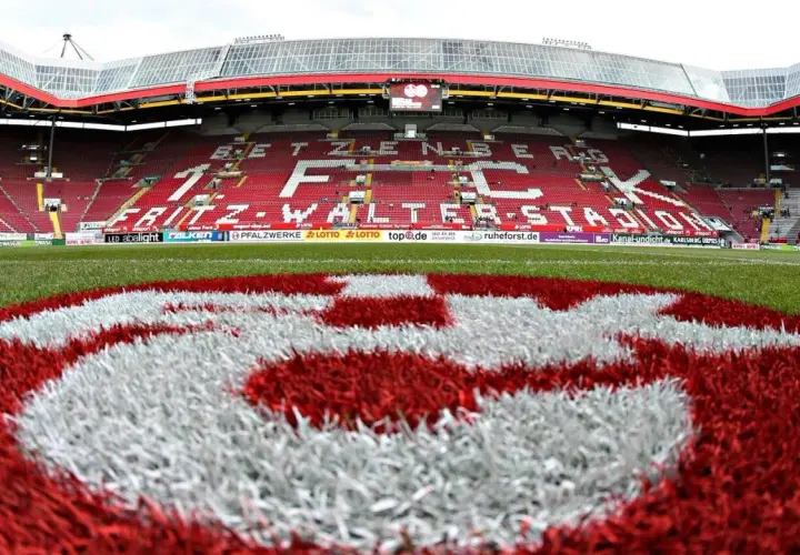 Na murawie stadionu Fritz-Walter-Stadion, symbol klubu FC Kaiserslautern. Czerwono-białe barwy drużyny dominują na trybunach i boisku.