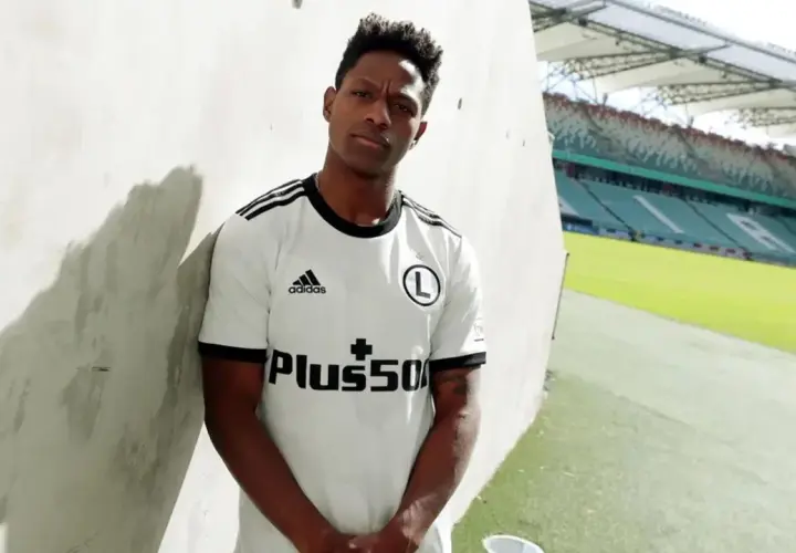 Joel Valencia w białej koszulce Legii Warszawa, z logo Plus500, na tle stadionu.