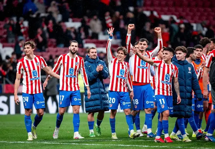 Piłkarze Atletico Madryt w pasiatych koszulkach świętują zwycięstwo. Wszyscy uśmiechnięci, niektórzy unoszą ręce w geście radości, kiedy gra Atletico Madryt przynosi sukces.