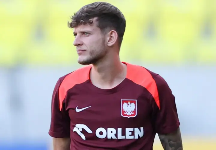 Piłkarz w bordowej koszulce z orłem, gdzie gra Szymański.