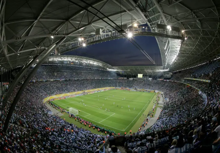 Widok z góry na pełny stadion Red Bull Arena Leipzig, gdzie tysiące kibiców w zielonych i niebieskich barwach dopingują swoje drużyny podczas nocnego meczu.