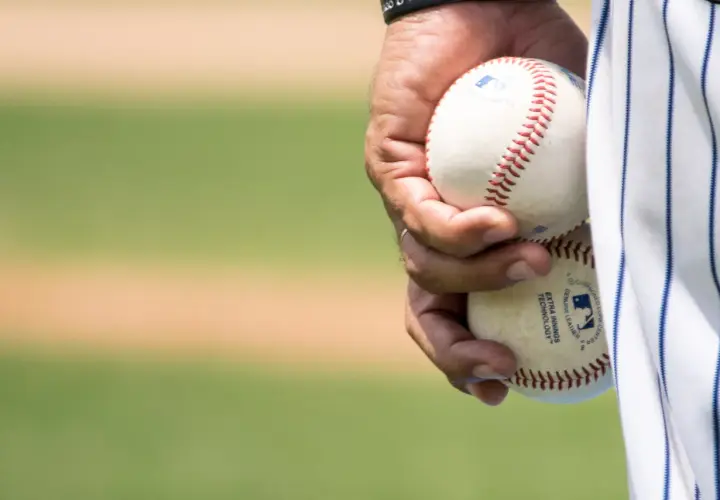 Dłoń trzyma dwie piłki baseballowe, gotowe do gry. Widać napis "EXTRA INNINGS TECHNOLOGY", świadczący o zaawansowanej technice niskiej piłki.