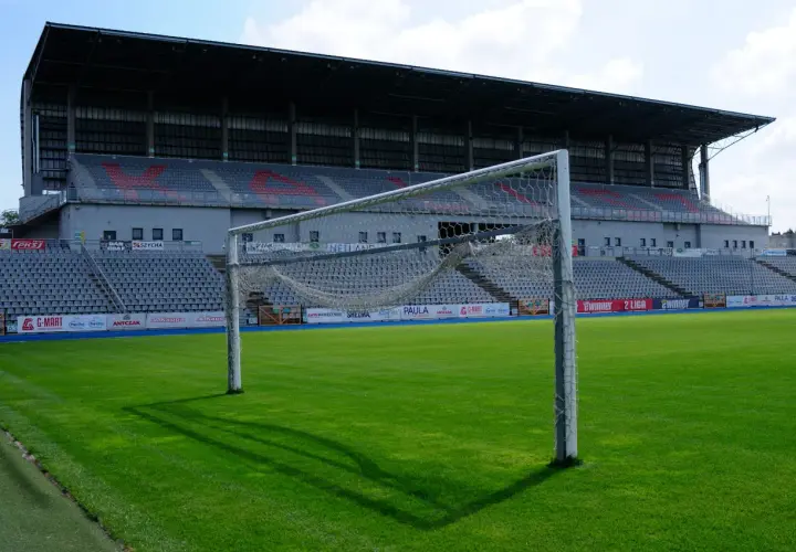Pusta bramka na zielonej murawie stadionu KKS Kalisz. W tle trybuny i zadaszenie.