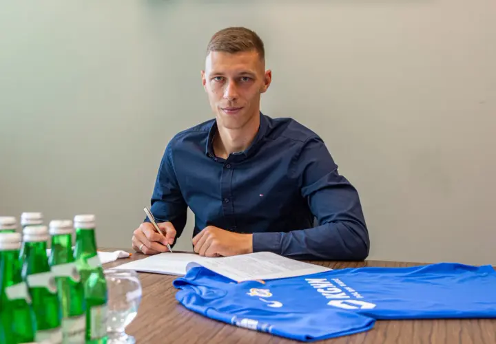 Dominik Hładun podpisuje kontrakt, obok leży niebieska koszulka.