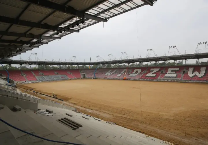 Trwa rozbudowa stadionu Widzewa. Na piaszczystym boisku widać prace budowlane i krzesełka w barwach klubu.