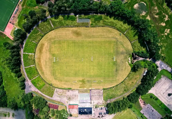 Widok z lotu ptaka na stadion Szombierki Bytom z zieloną murawą, trybunami i otaczającą go zielenią.
