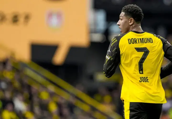 Piłkarz Jobe Bellingham w żółtej koszulce z numerem 7 i napisem "DORTMUND" na plecach, na tle trybun.