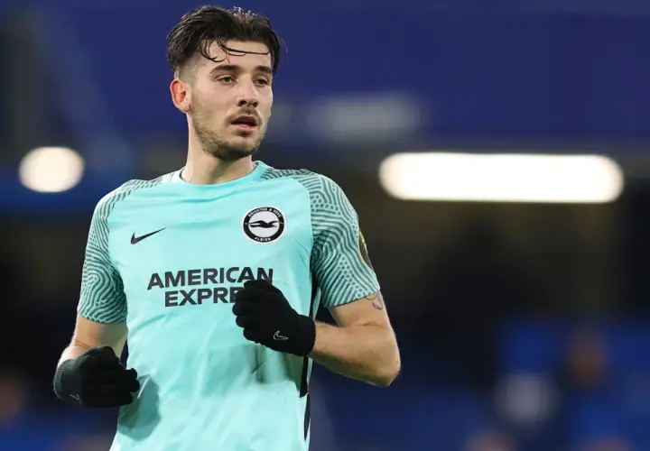 Piłkarz Jakub Moder w koszulce Brighton, zmagający się z kontuzją, na tle niebieskich trybun.