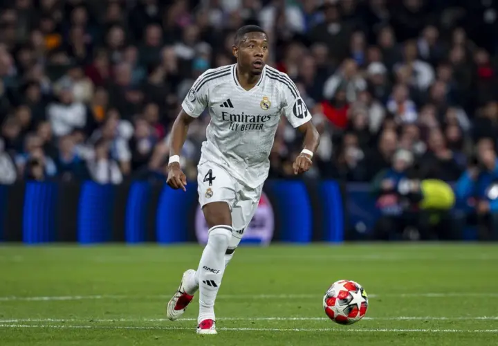 David Alaba w białej koszulce Realu Madryt z numerem 4 biegnie z piłką na murawie, skupiony na grze.