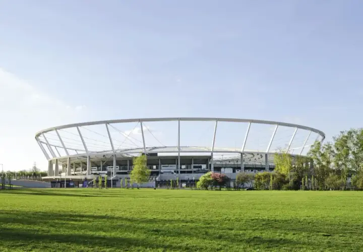 Nowoczesny Stadion Śląski otoczony zielenią, z charakterystyczną, okrągłą konstrukcją dachu.