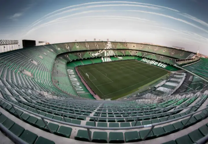 Puste trybuny stadionu Real Betis, zielone krzesełka tworzą mozaikę pod błękitnym niebem.