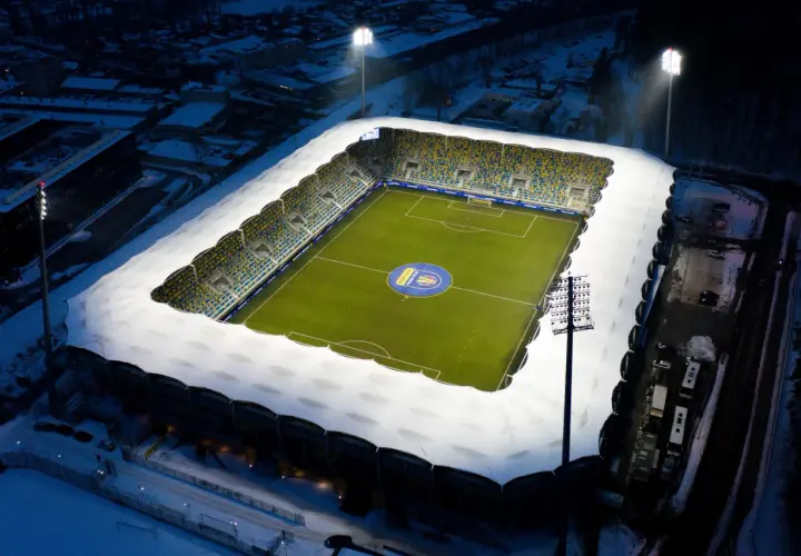 Zimowy wieczór na stadionie Gdynia Arka. Oświetlony stadion z zieloną murawą i śniegiem na trybunach, gotowy na mecz Bałtyk Gdynia.