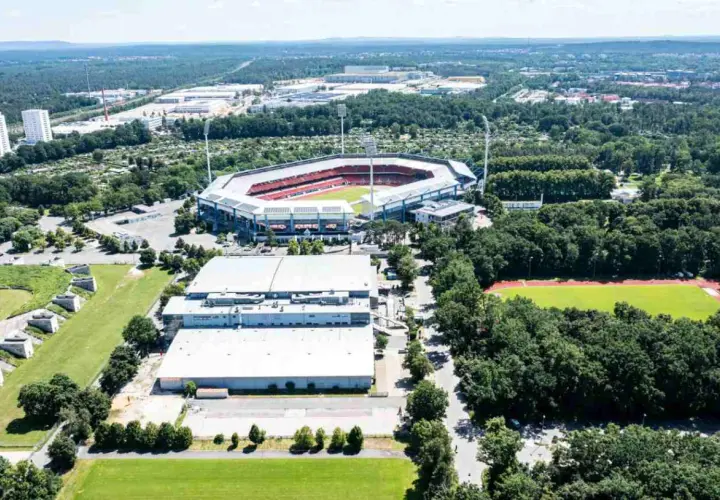 Widok z lotu ptaka na Max-Morlock-Stadion otoczony zielenią, z pobliskimi budynkami i boiskiem sportowym.