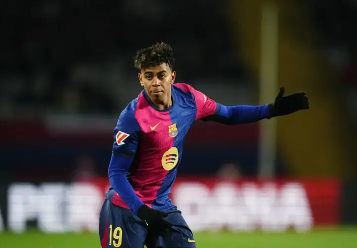 Młody zawodnik FC Barcelona w charakterystycznej koszulce, z numerem 19 na spodenkach, gestykuluje na boisku.