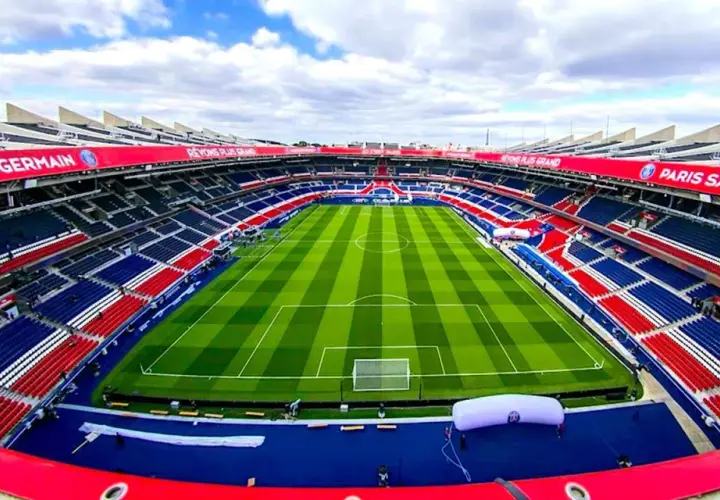 Pusta trybuna stadionu Parc des Princes, z czerwono-niebieskimi siedzeniami i zieloną murawą, gotowa na mecz Paris Saint-Germain.