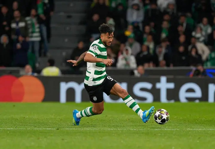 Piłkarz Sporting CP w zielono-białej koszulce drybluje z piłką na boisku.
