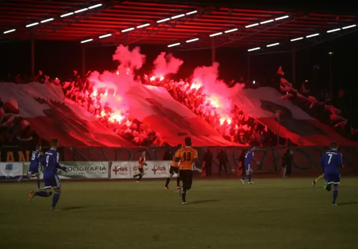 Chrobry Głogów stadion w ogniu rac! Kibice tworzą biało-czerwoną oprawę, a piłkarze grają na murawie.