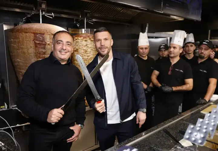 Lukas Podolski z nożami w ręku, obok niego pracownicy jego restauracji z kebabem.