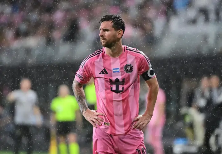 Lionel Messi w różowej koszulce Interu Miami, stojący w deszczu. Wygląda na zamyślonego, być może z powodu niedawnej kontuzji.