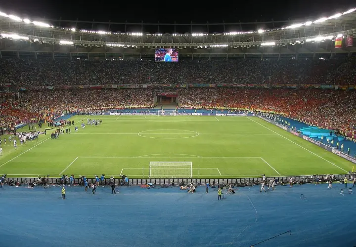 Piłkarze wychodzą na murawę stadionu olimpijskiego w Kijowie. Tłumy kibiców na trybunach, wielki ekran nad boiskiem.