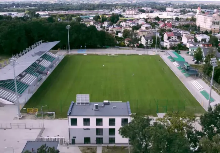 Stadion Wisłoki Dębica z zieloną murawą i trybunami, otoczony drzewami i zabudowaniami miejskimi.