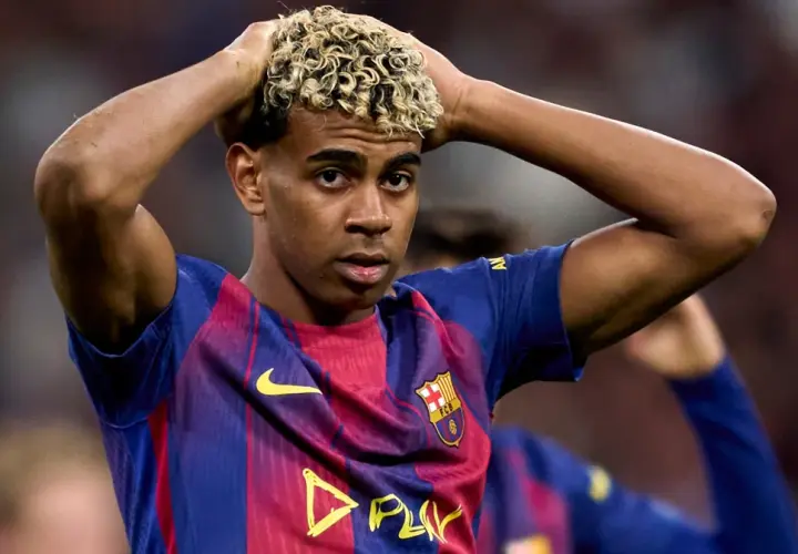 Młody piłkarz Lamine Yamal w koszulce FC Barcelona z blond lokami, trzymający się za głowę.