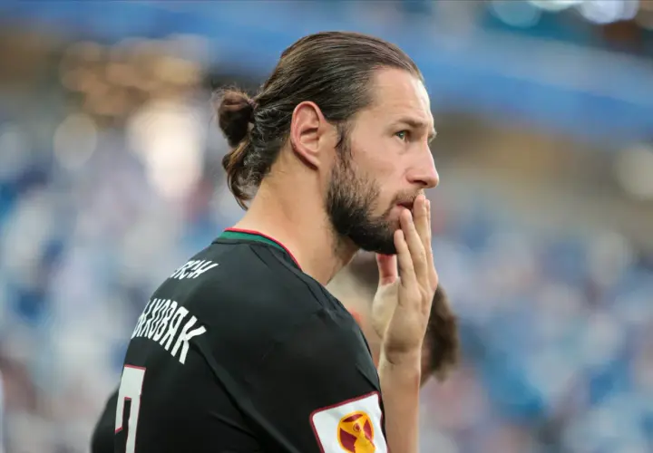 Grzegorz Krychowiak w czarnej koszulce, z włosami związanymi w kok, zamyślony na boisku.