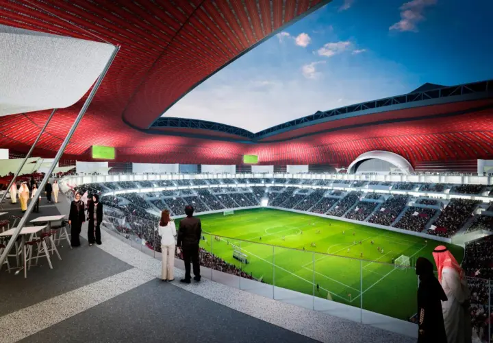 Widok na zieloną murawę stadionu Al Bayt, otoczoną trybunami pełnymi widzów. Czerwony dach tworzy imponującą konstrukcję.