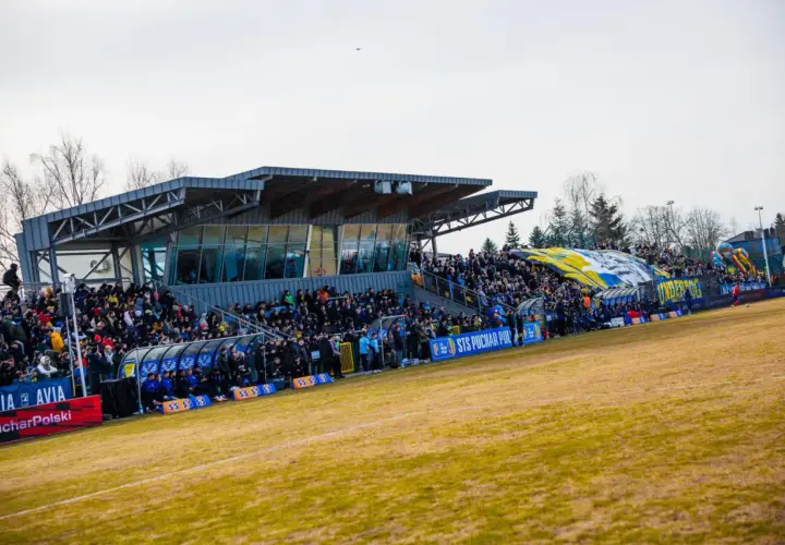 Widok na trybuny stadionu Avia Świdnik, wypełnione kibicami. W tle widać zadaszenie i drzewa.
