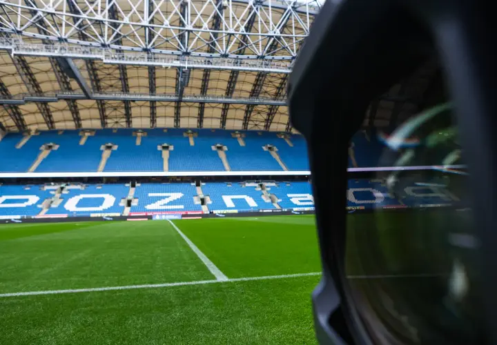 Pusta trybuna stadionu Lecha Poznań. Widoczne niebieskie sektory i miejsca, zielona murawa.