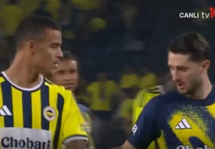 Piłkarze w żółto-granatowych strojach, jeden z nich to Mason Greenwood, rozmawiają na boisku.