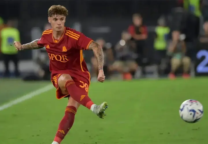 Nicola Zalewski w akcji, kopie piłkę na boisku w czerwonej koszulce AS Roma.