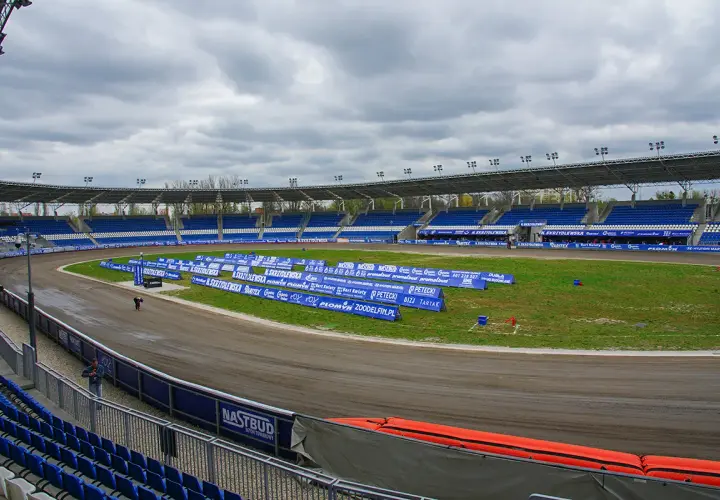 Pusty stadion żużlowy Orzeł Łódź z niebieskimi trybunami i torem żużlowym.
