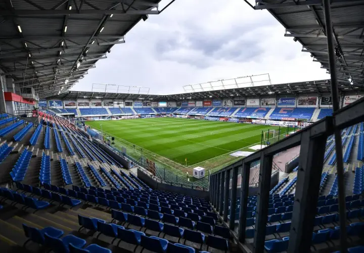 Puste trybuny stadionu Piasta Gliwice czekają na kibiców. Zielona murawa boiska lśni w blasku dnia.