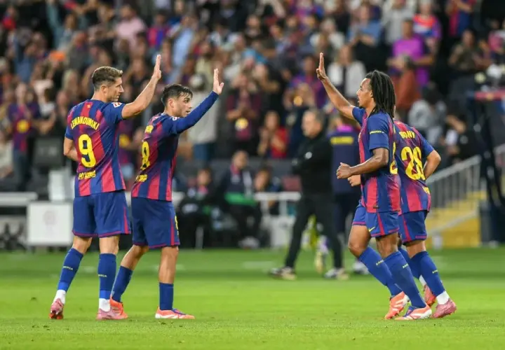 Piłkarze FC Barcelona świętują zwycięstwo w rozgrywkach. Lewandowski, Pedri i Koundé podnoszą ręce w geście radości na boisku.