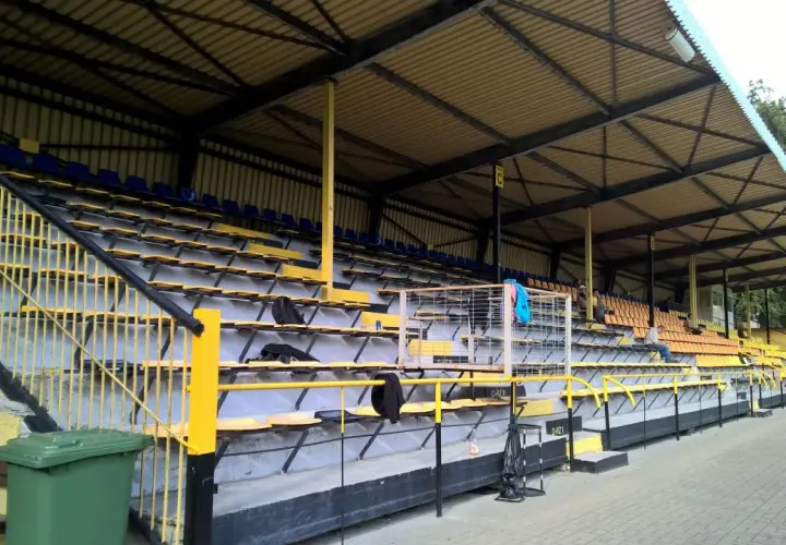 Puste trybuny stadionu Gryf Wejherowo, z żółtymi i niebieskimi siedzeniami pod zadaszeniem.