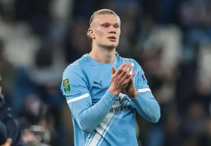 Erling Haaland w błękitnej koszulce Manchesteru City, z pucharem Carabao Cup na rękawie, klaszcze na boisku.