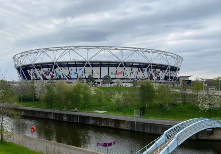 Ogromny stadion West Ham United z charakterystycznym logo klubu, otoczony zielenią i kanałem wodnym.