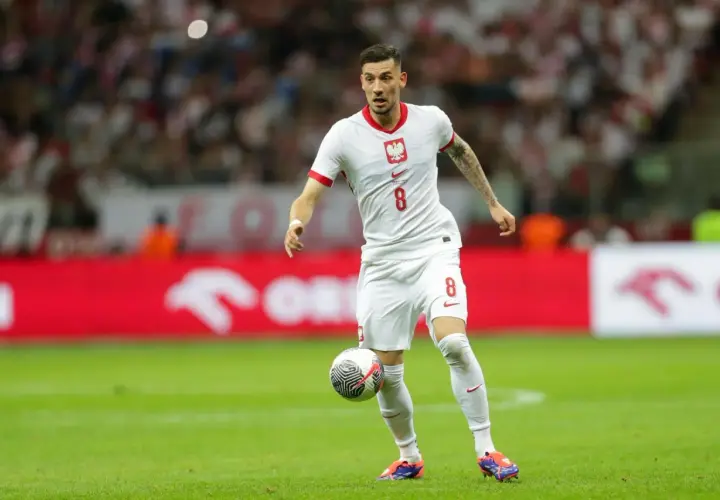 Jakub Moder w białej koszulce z numerem 8, z piłką przy nodze na boisku.
