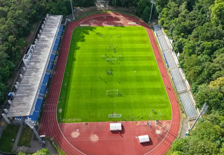Piłkarze trenują na zielonej murawie stadionu Floty Świnoujście, otoczonego drzewami.