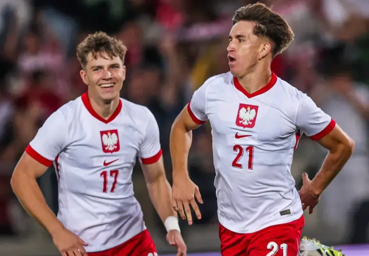 Dwóch młodych zawodników w białych koszulkach z orłem na piersi, z numerami 17 i 21, cieszy się po zdobytej bramce.